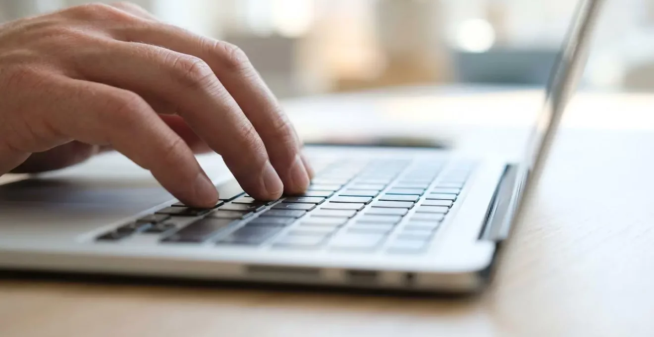 Fotografía macro de una mano tecleando en un ordenador portátil moderno con enfoque selectivo en las teclas y fondo desenfocado